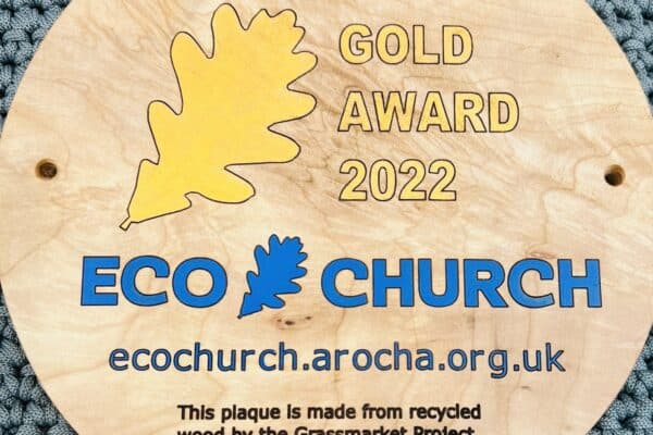 A wooden circular plaque reading "A Rocha Gold Award 2022 and the Eco Church logo