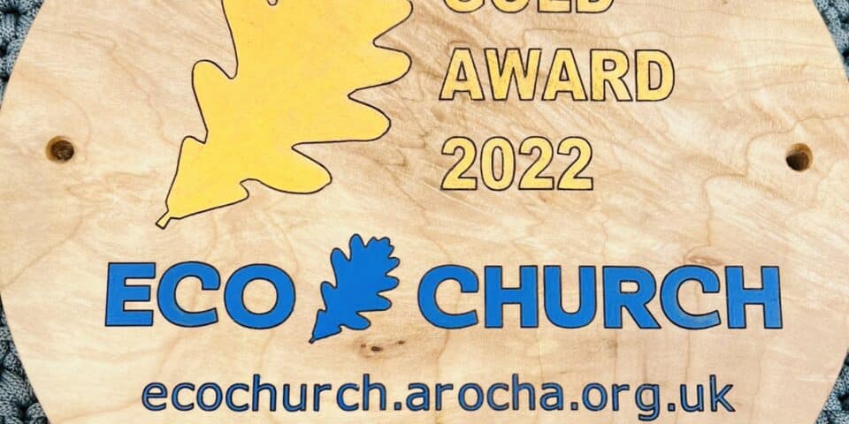 A wooden circular plaque reading "A Rocha Gold Award 2022 and the Eco Church logo