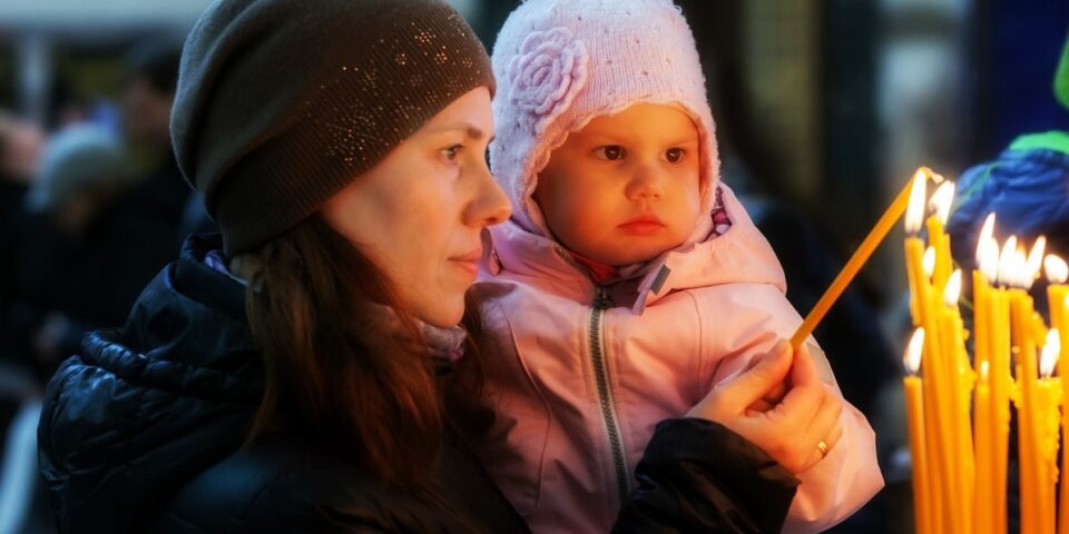 Mother with daughter lighting a candle in church