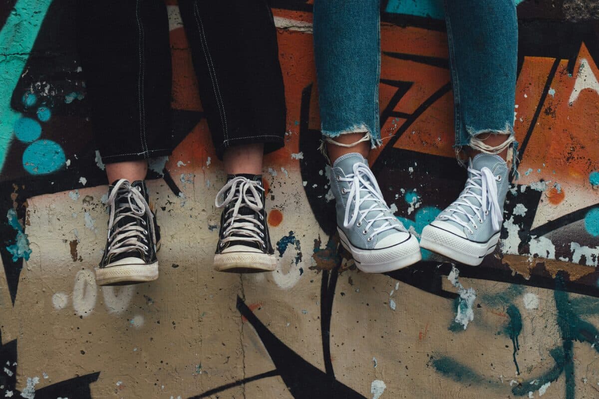 teenagers feet as they sit against a graffitied wall