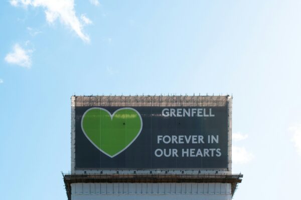 Grenfell Tower covered in white tarpaulin with Grenfell United logo at the top.