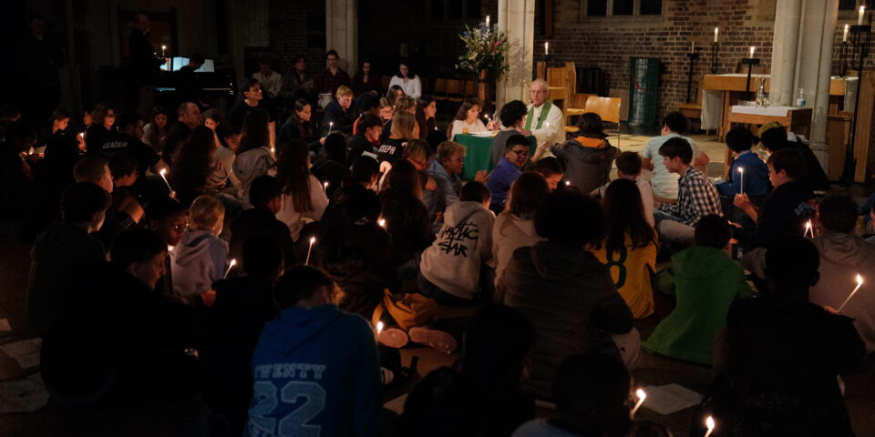 A photo of a candlelit service where communion is taking place. The Archbishop of Canterbury is presiding on a low altar, surrounded by young people on the floor and dais.