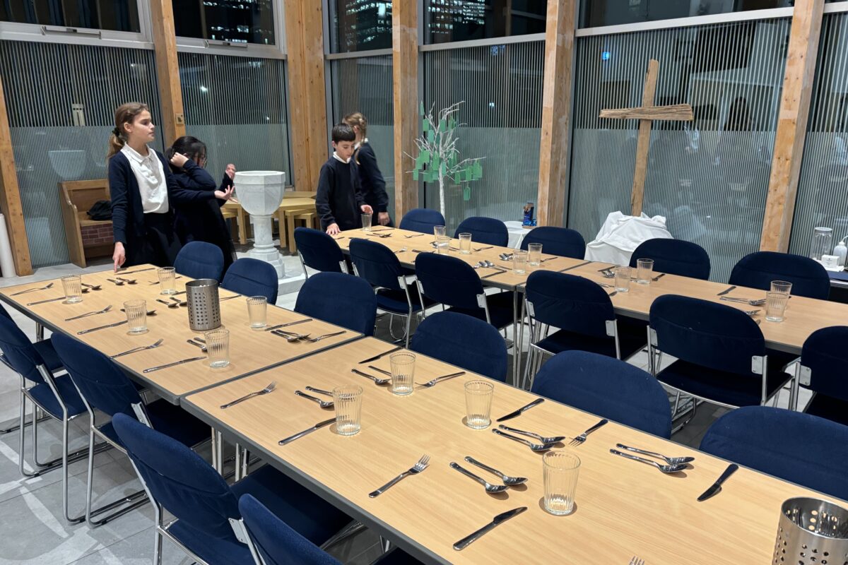 children in a church room with glass walls, setting up a table for dinner