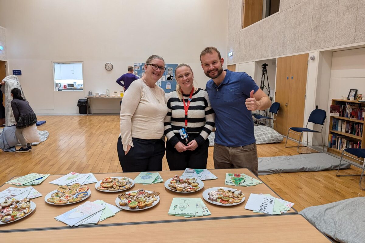 Three adults smiling to camera in a church hall being set up for a night shelter