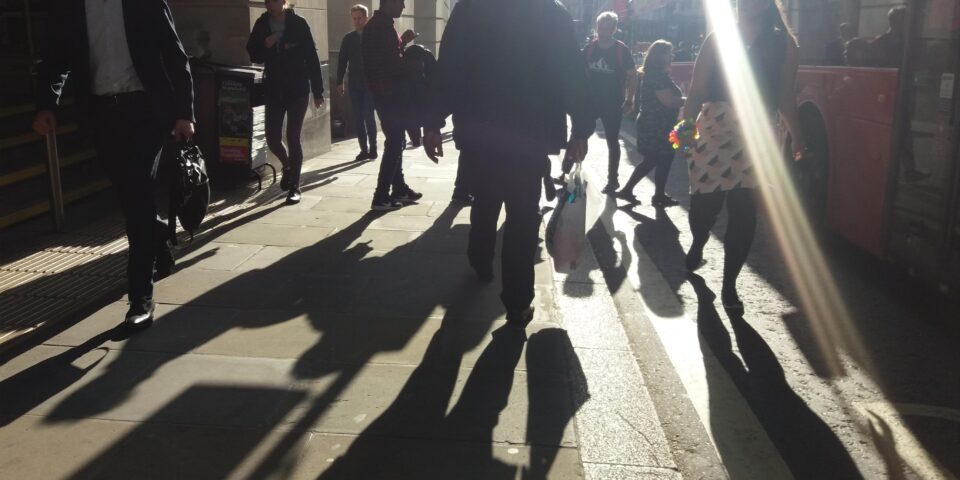 a bustling london street with bright sun and shadows of pedestrians, alongside a London bus