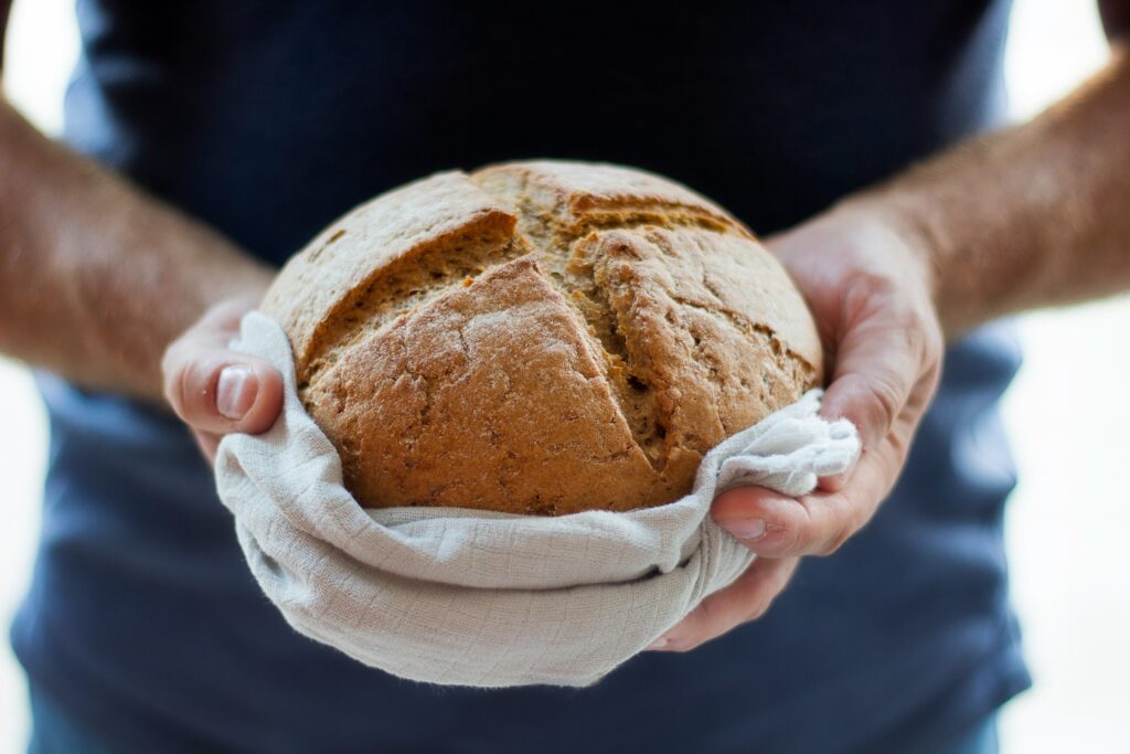 a round loaf of fresh bread with a cross scored across the top, being held in two hands