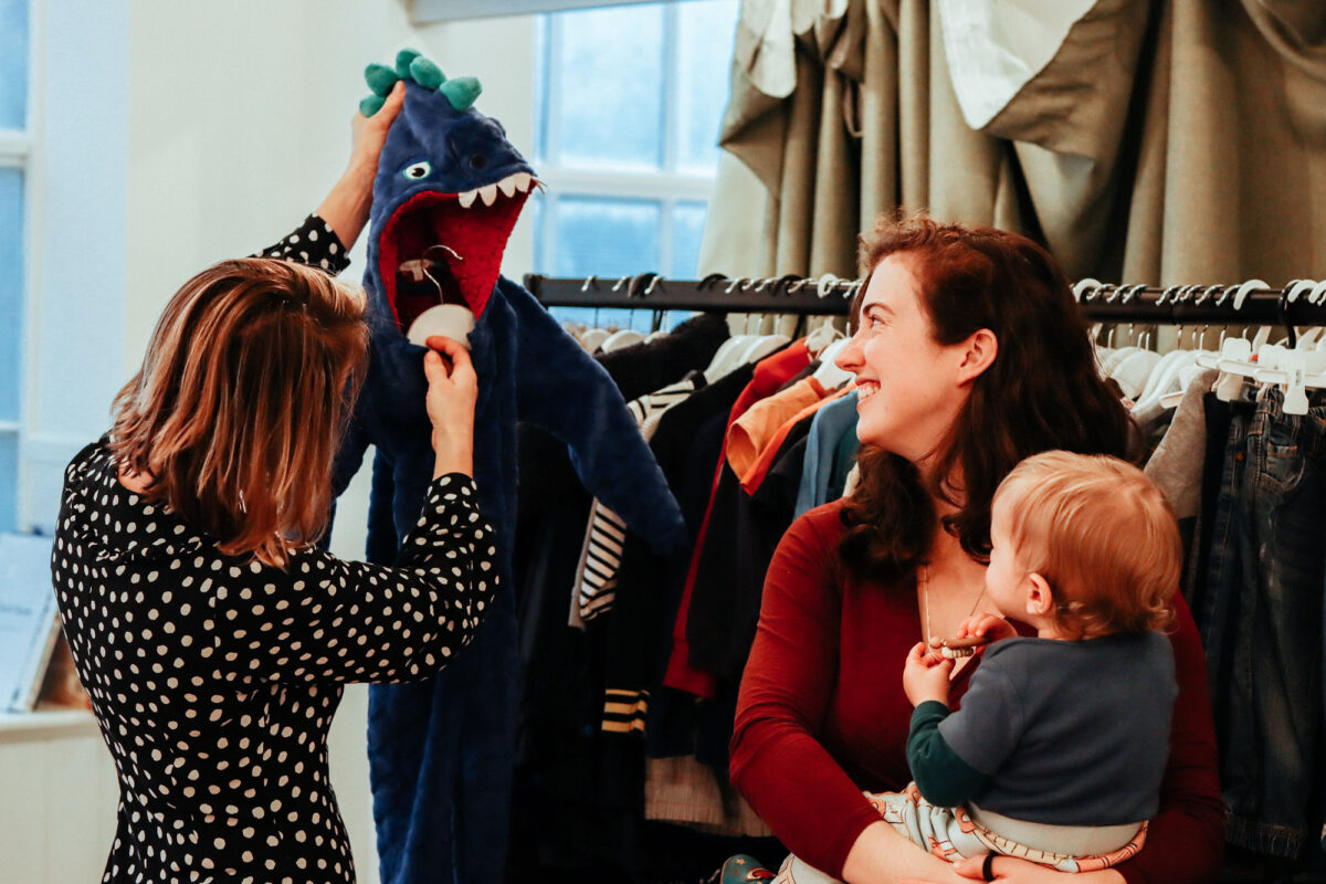A Choices staff member holds up a dinosaur onesie for a mum and baby in the KXC Boutique.