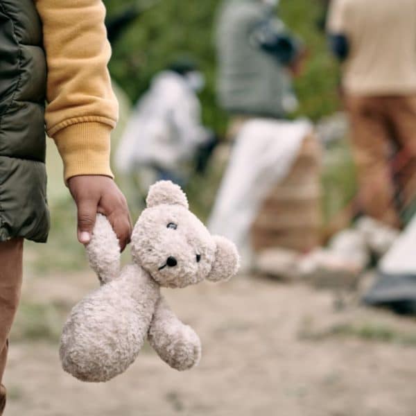 Close-up of a child holding a teddy bear at a temporary tent settlement for refugees.