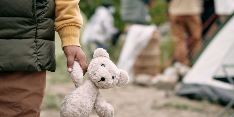 Close-up of a child holding a teddy bear at a temporary tent settlement for refugees.
