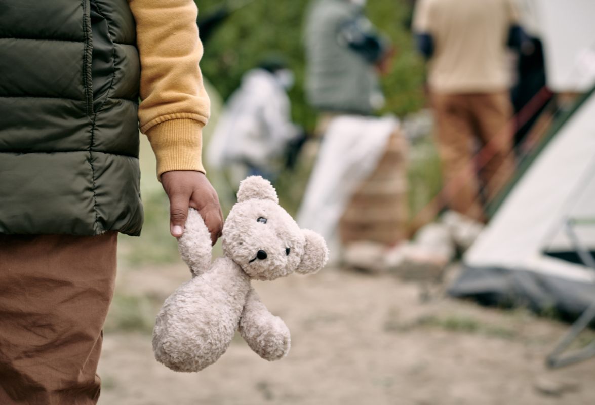 Close-up of a child holding a teddy bear at a temporary tent settlement for refugees.